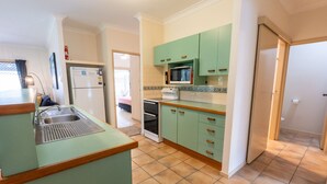 Een kleine keuken met groene kastjes, een spoelbak, een magnetron en een oven.