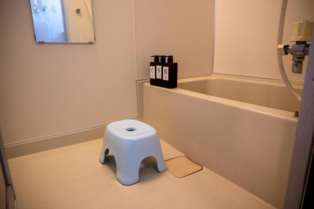 A bathroom with a white bathtub, a small white stool, and two black bottles on the wall.