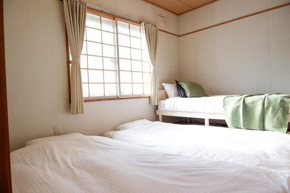 A bedroom with two beds, a window with curtains, and a wooden ceiling.