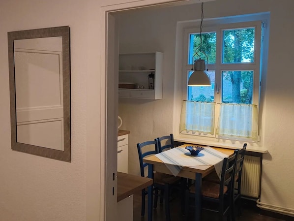 Un comedor con una mesa y sillas, una ventana con vistas a árboles y una lámpara colgante.