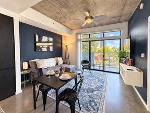 A modern living room with a dining area, large windows, and a ceiling fan.