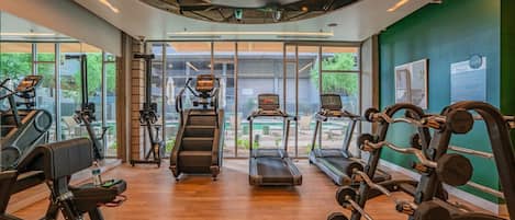 A gym with cardio equipment, weight machines, and a large window providing a view of the outdoors.