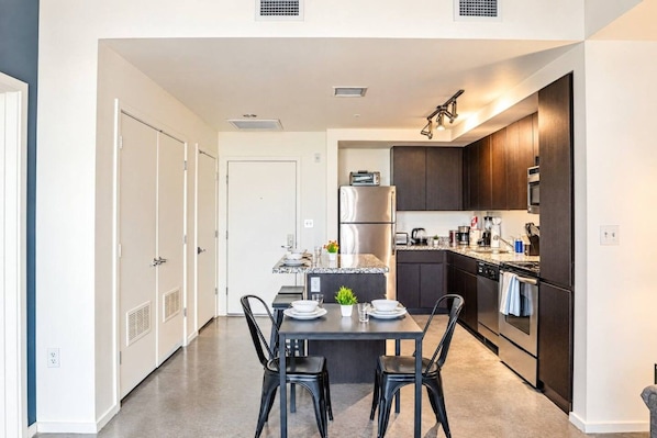 A modern kitchen with dark cabinetry, a central island with seating, and a dining area with a table and chairs.