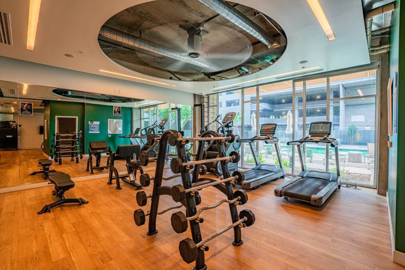 Et fitnesscenter med løbebånd, styrketræningsudstyr og et stort vindue med udsigt over naturen.