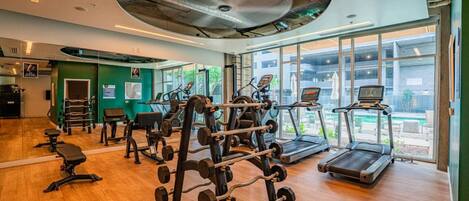 Une salle de sport équipée de machines de cardio, de matériel de musculation et dotée d’une grande fenêtre offrant une vue sur l’extérieur.