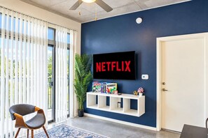 A room with a large flat-screen TV mounted on a dark blue wall, a white door, and a white console table with board games. - Phoenix Arts District Escape | Pool, Gym & Parking (Phoenix)