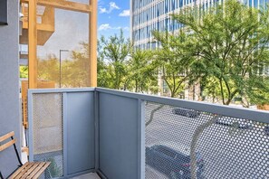 A balcony with a mesh railing, a wooden bench, and a view of a modern building and trees.