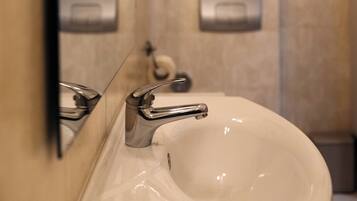 A bathroom with a white sink, a mirror, and a towel dispenser.