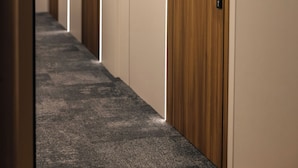 Un pasillo con puertas de madera, piso alfombrado e iluminación empotrada.