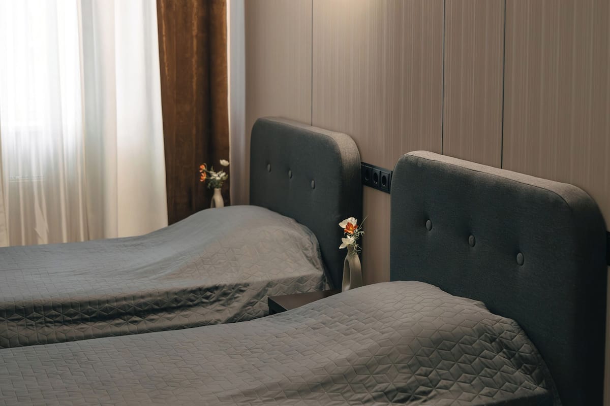 A bedroom with two beds, a wall-mounted light, and a window with curtains.