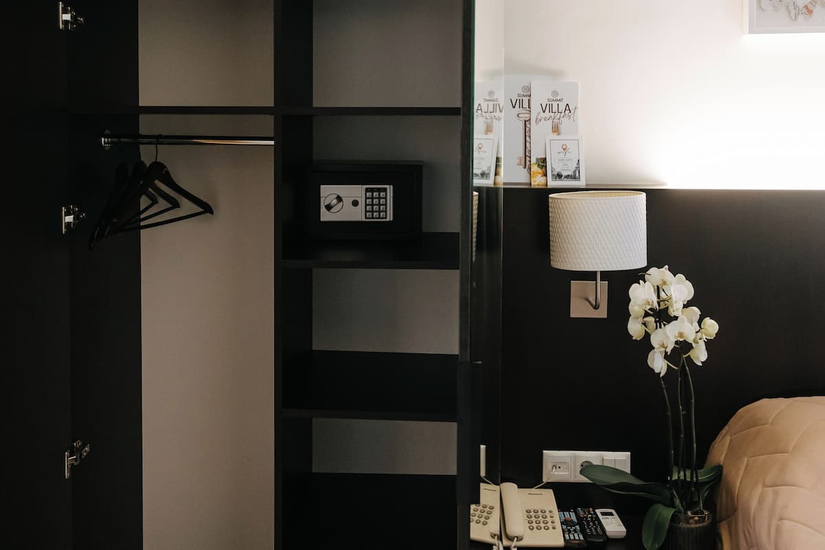 A modern hotel room with a black wardrobe, a bedside table with a lamp, a phone, and a plant.