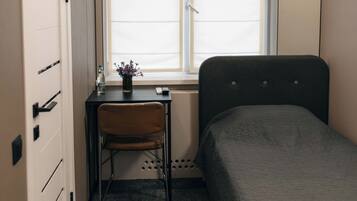 A compact room with a bed, a desk with a chair, a window, and an air conditioning unit.
