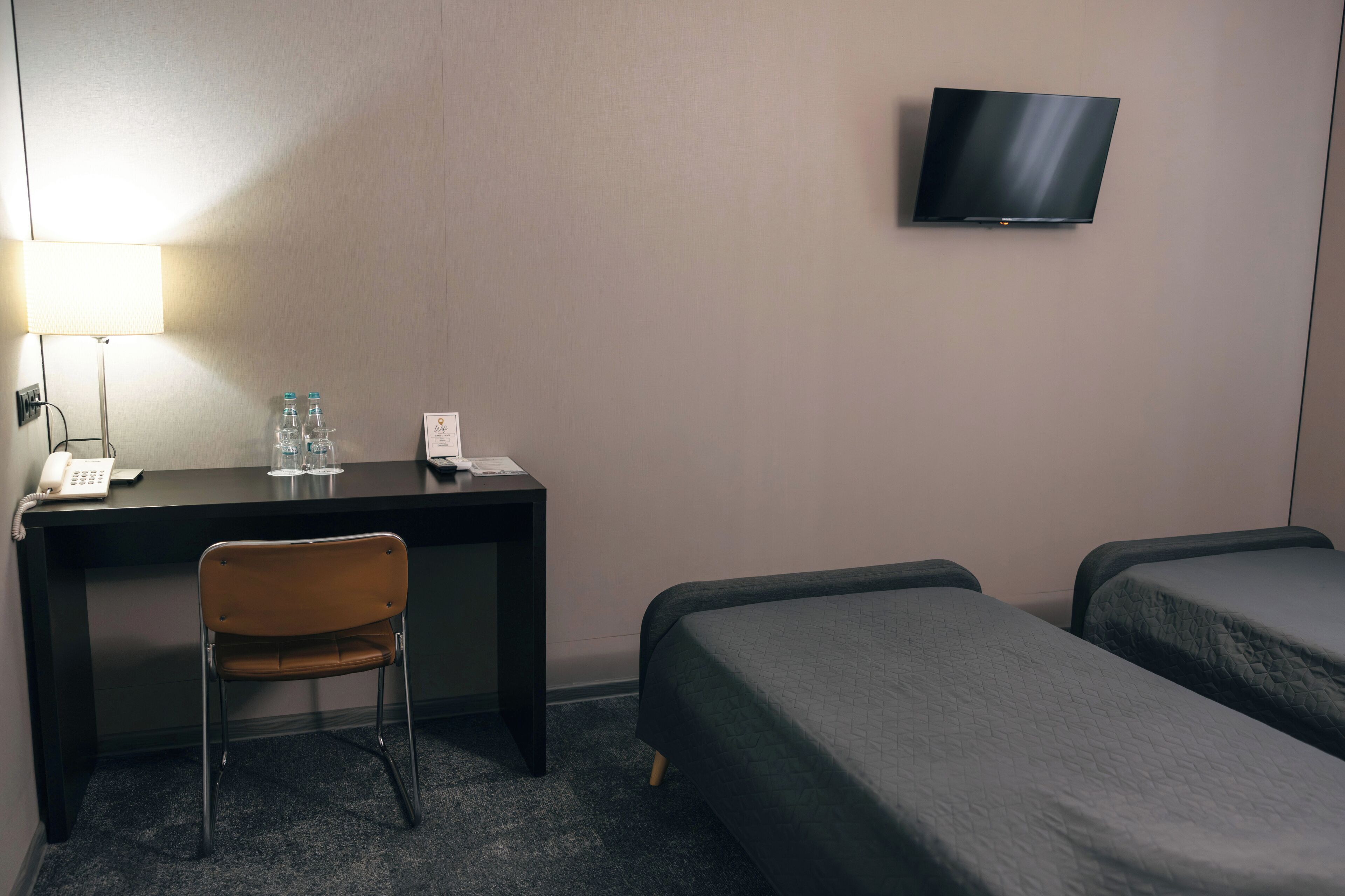 Une chambre d’hôtel équipée d’un bureau, d’une chaise, de deux lits, d’une télévision et d’une lampe.
