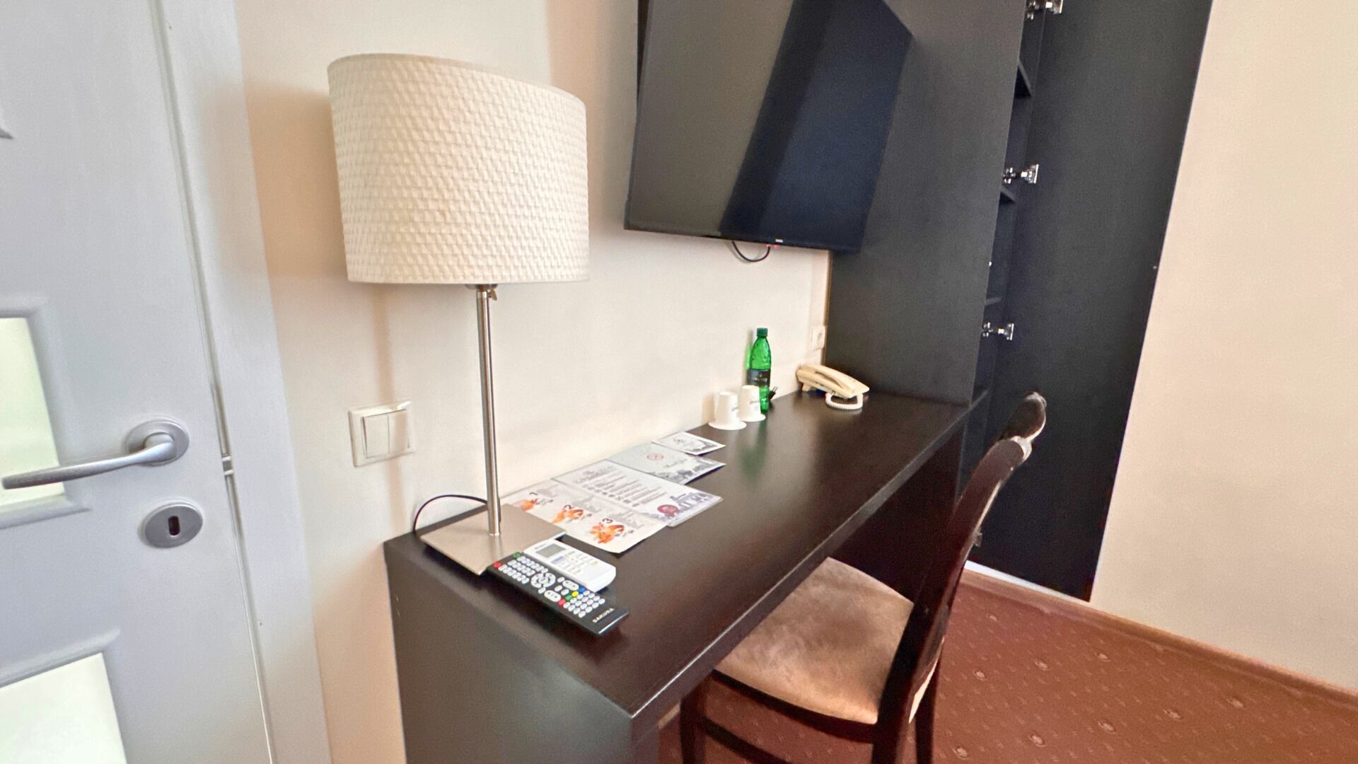 A hotel room with a desk, a lamp, a TV, and a chair.