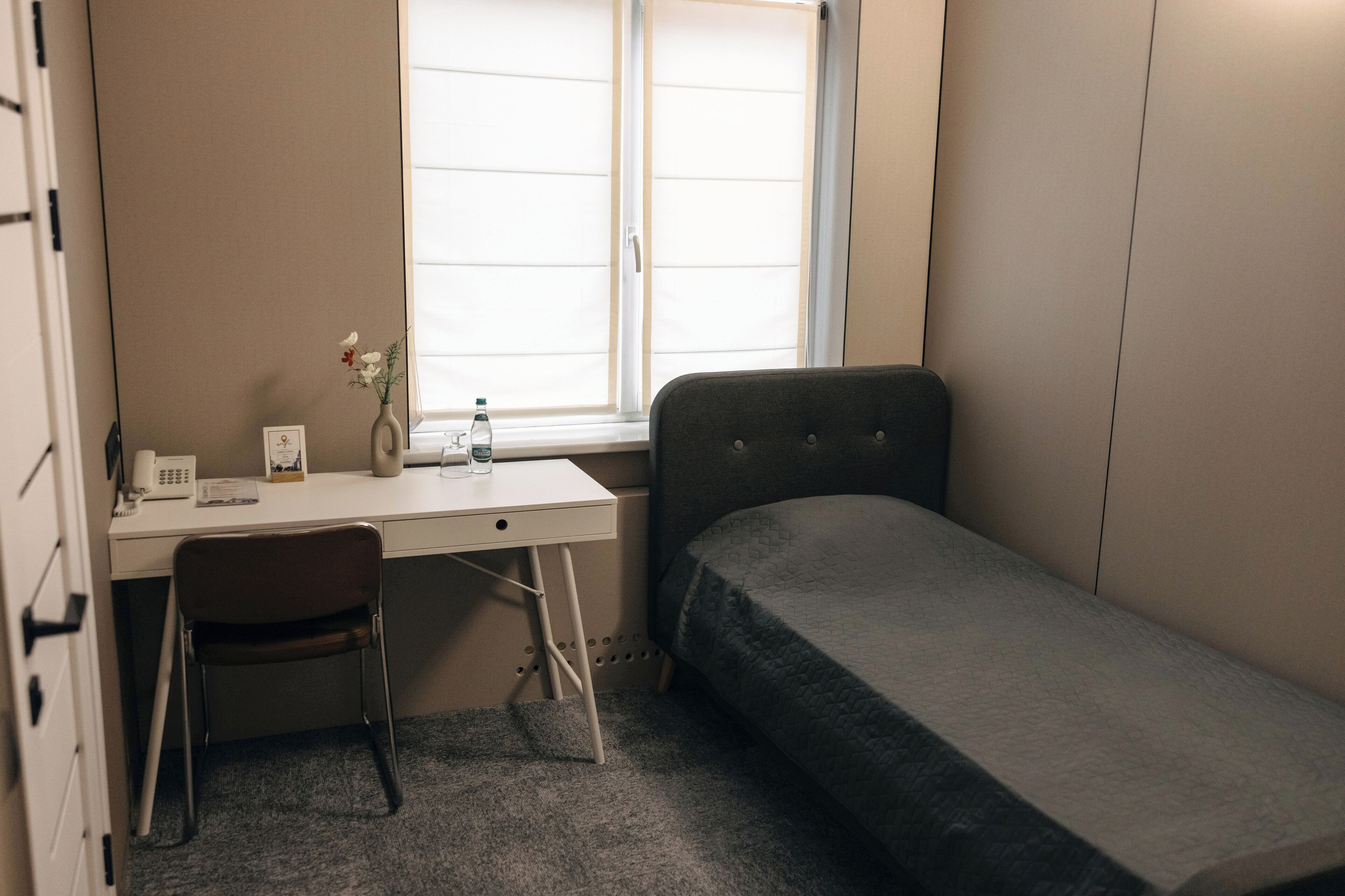A small, compact room with a single bed, a desk with a chair, a window, and a radiator.
