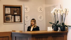Un mostrador de recepción con detalles de madera, un reloj que muestra horarios para Chisinau, Nueva York, Berlín y Londres, y una orquídea en maceta.