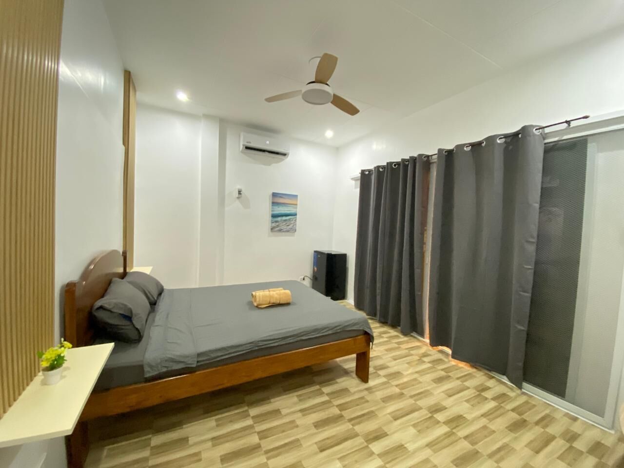 Ein Schlafzimmer mit Bett, Deckenventilator, Klimaanlage, Lautsprecher und einem Fenster mit Vorhängen.