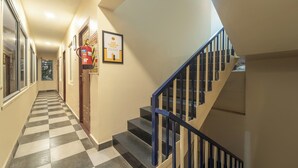 A hotel hallway with a checkered floor, a fire extinguisher, and a staircase with blue railings. - Itsy Hotels Everest Leela Residency (Erode)
