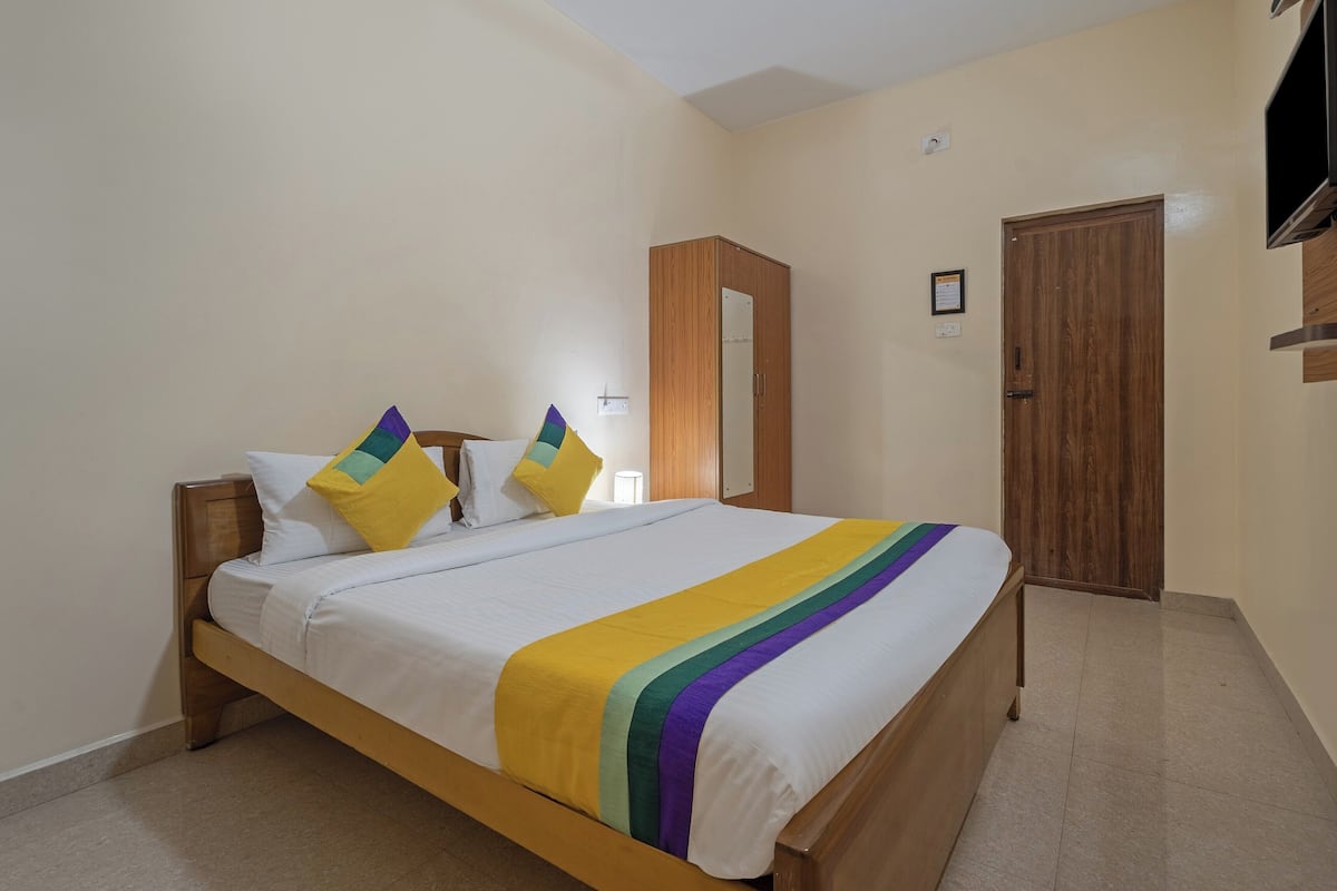 Una cama bien tendida con una colcha a rayas de arcoíris y dos almohadas, un armario de madera, una puerta y un televisor montado.