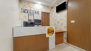 A hotel reception desk with a wooden finish, a mounted flat-screen TV, and a sign for 'EVERES' hotels. - Itsy Hotels Everest Leela Residency (Erode)