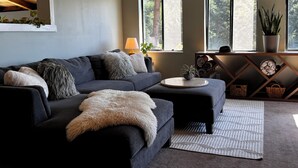 Un salon moderne avec un canapé gris foncé, une table basse ronde et une grande fenêtre donnant sur la verdure.