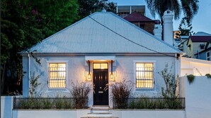 Een huis met twee verdiepingen, een puntige dak, een voordeur met een zwart deurpaneel en glas, en twee verlichte ramen.