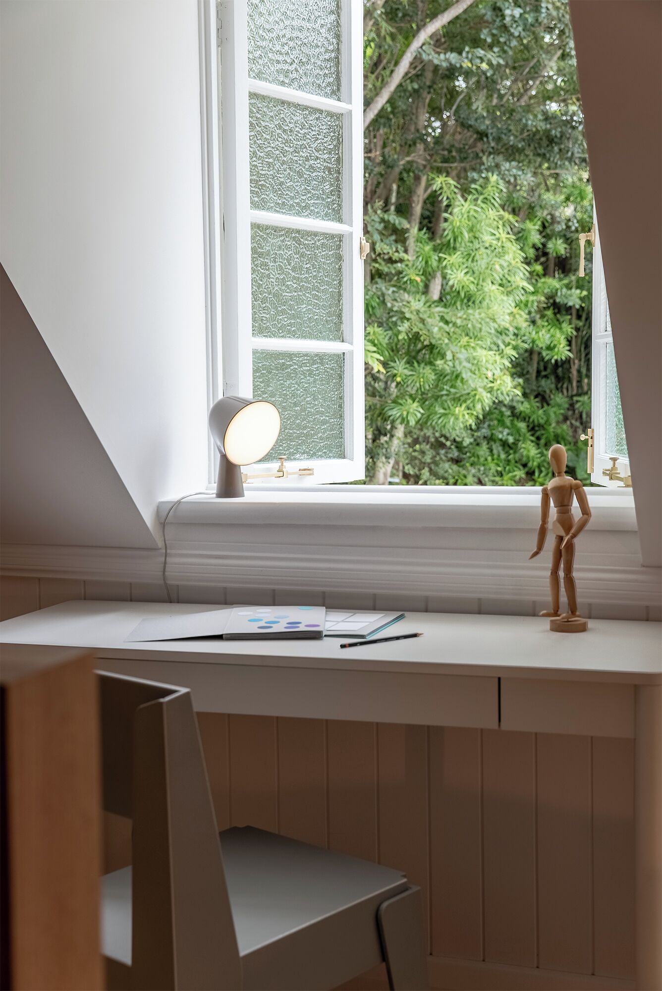 Ett arbetsområde med ett skrivbord, en skylldocka och ett fönster med utsikt över grönområden.