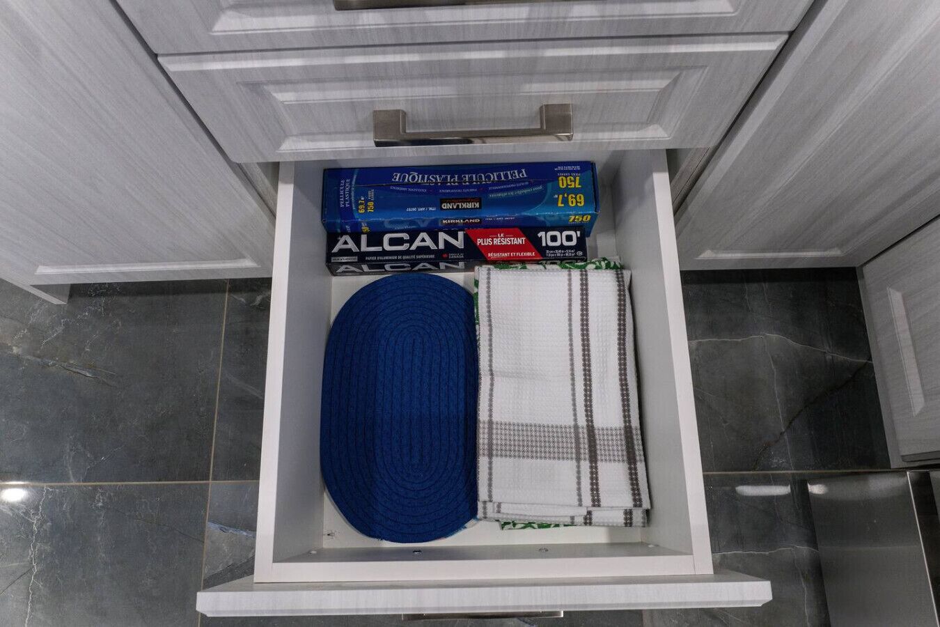 A bathroom with a white shelf holding a blue towel, a white towel, and two boxes of Alcan Plus Resistant 100 tissue.