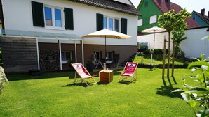 Une maison dotée d’un patio comprenant deux chaises longues et une table, le tout installé sous un grand parasol.