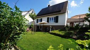 Une maison dotée d’un toit recouvert de panneaux solaires, d’une pelouse bien entretenue et d’un patio aménagé avec une table et des chaises.