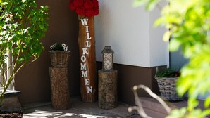 Une enseigne en bois portant l’inscription « WILLKOMMEN » et ornée d’une fleur rouge, un panier en osier et une lanterne posée sur un socle en pierre.