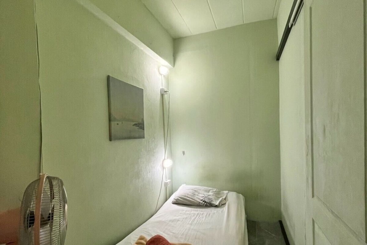 A narrow room with a bed, a standing fan, and a nightstand.