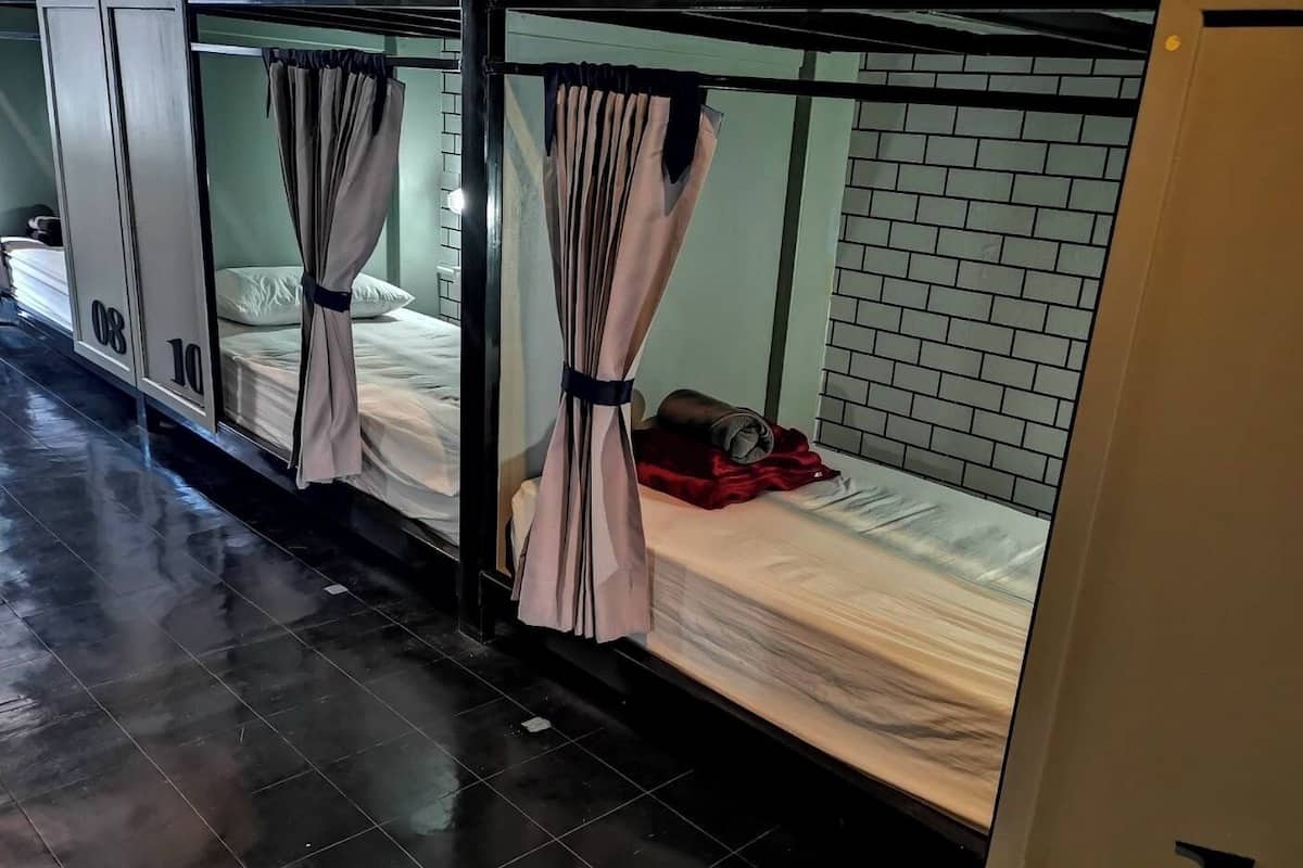 A row of bunk beds with curtains, a tiled floor, and a brick wall in the background.