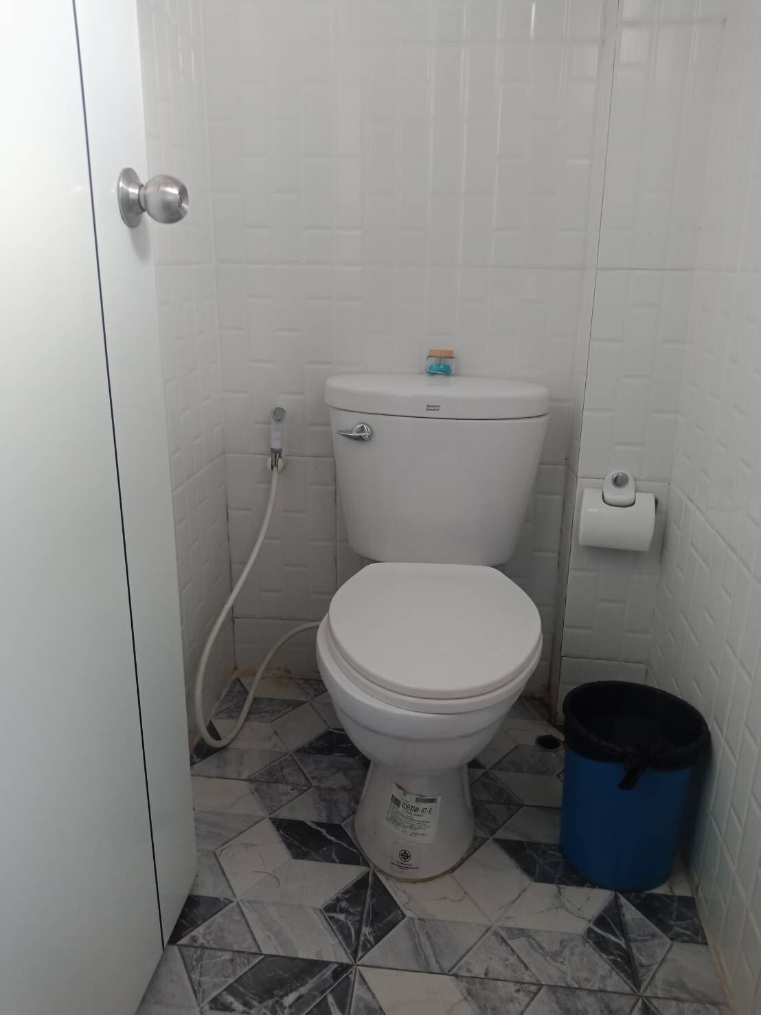 Un baño pequeño con un inodoro, un bote de basura azul y un dispensador de papel higiénico en la pared.