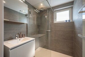 A modern bathroom with a glass-enclosed shower, a white sink, and a window providing natural light.