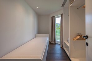 A minimalist bedroom with a single bed, a sliding door leading to a balcony, and a coat rack.