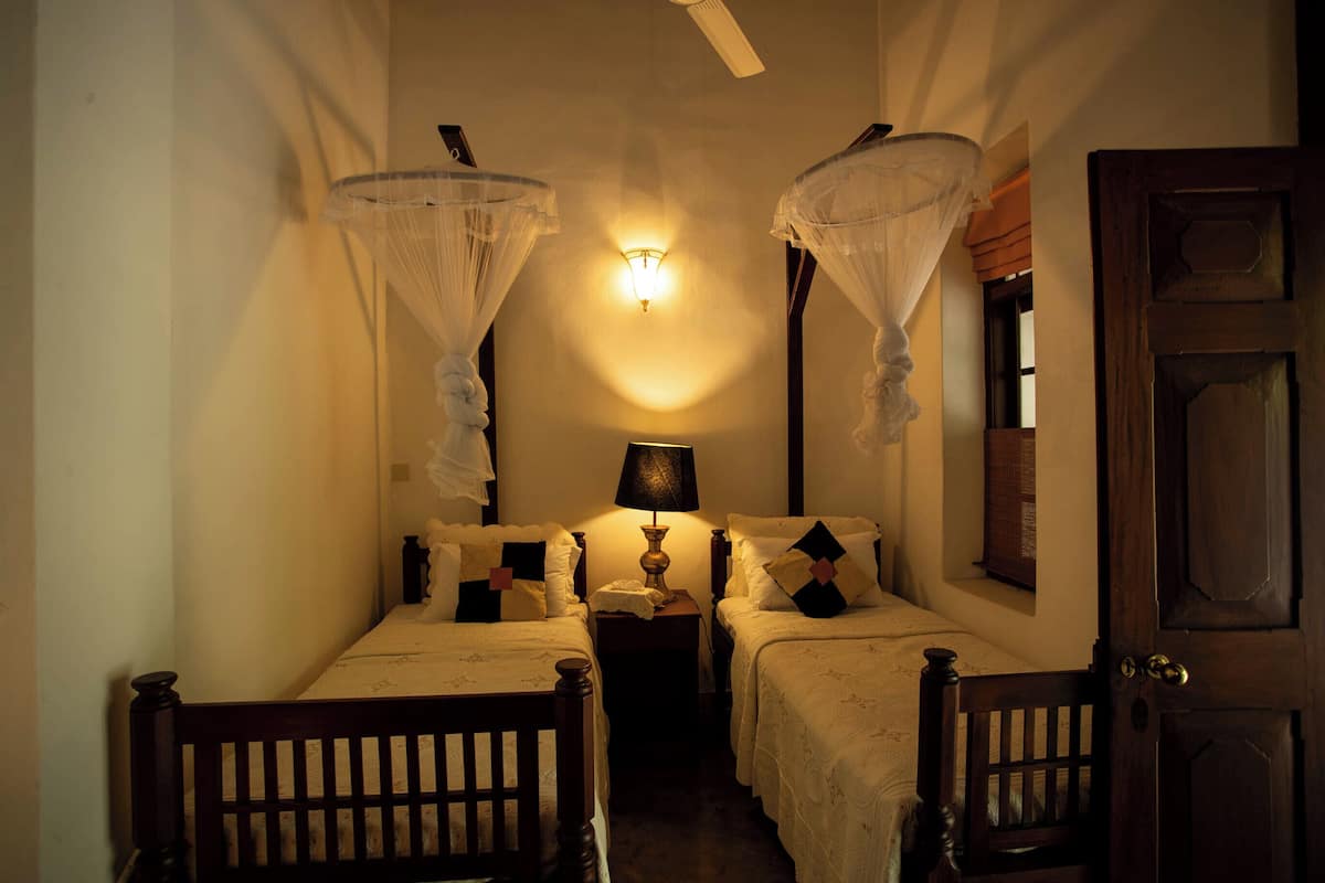 A room with two beds, a nightstand, a lamp, and a door.