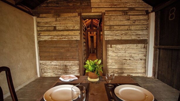 A rustic wooden dining area with a table set for two, a potted plant, and a wooden door in the background. - Eladetta Retreats  (Kandy)