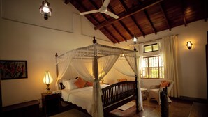 A four-poster bed with a canopy, a bedside table with a lamp, a chair, and a view of the outdoors through a window. - Eladetta Retreats  (Kandy)