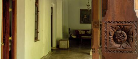 A wooden door with intricate carvings, a hallway leading to a room with a chair and a painting on the wall.