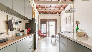 Een moderne keuken met grijze kastjes, een houten aanrechtblad en een rode stoel. Een eethoek met een tafel en stoelen is zichtbaar door een geopende deur.