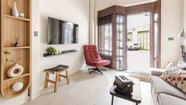 Een moderne woonkamer met een flatscreen televisie, een rode fauteuil, een houten plank met decoratieve objecten en uitzicht op de straat.