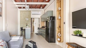Een knus woongedeelte met een kitchenette, een bank, een salontafel en een aan de muur bevestigde televisie.