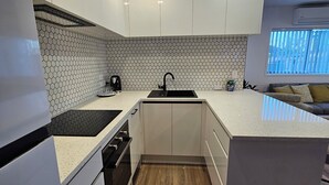 Een moderne keuken met witte kasten, een zwart aanrecht en een achterwand van honingraatmozaïek.