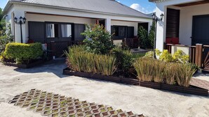 A two-story building with a flat roof, a covered porch, and a garden area with various plants and a paved walkway.