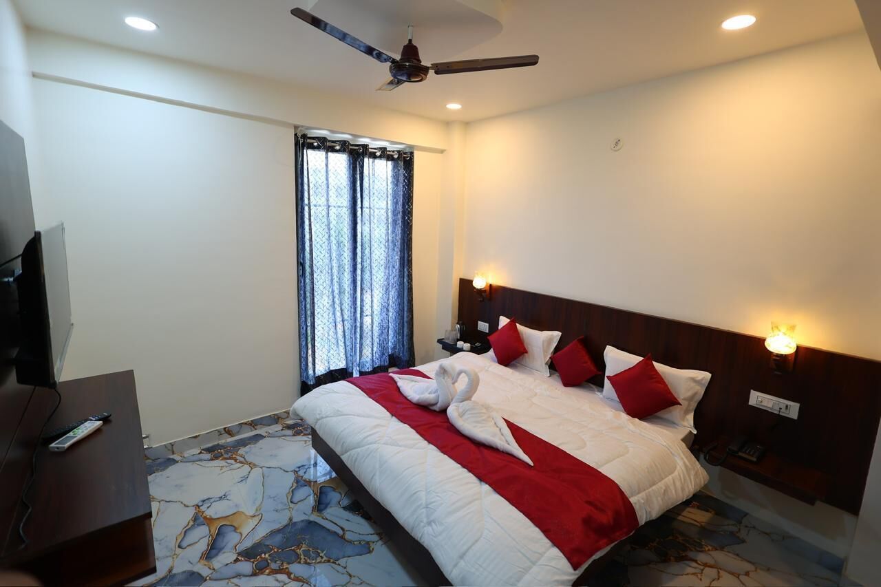 A hotel room with a bed, a ceiling fan, a TV, and a window with curtains.