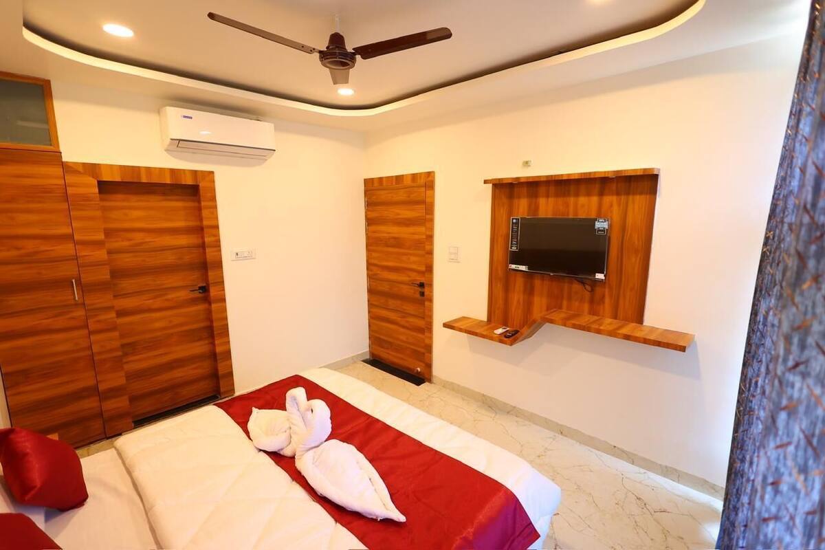 A hotel room with a bed, a ceiling fan, an air conditioning unit, wooden wardrobes, and a mounted TV.