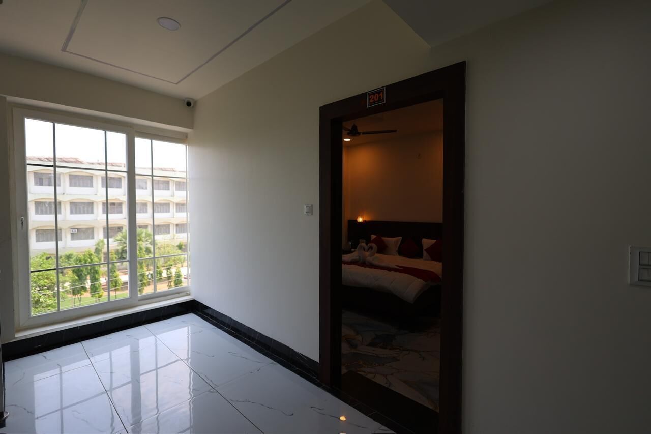 A hotel room with a large window, a bed with white bedding, and a dark wooden door.