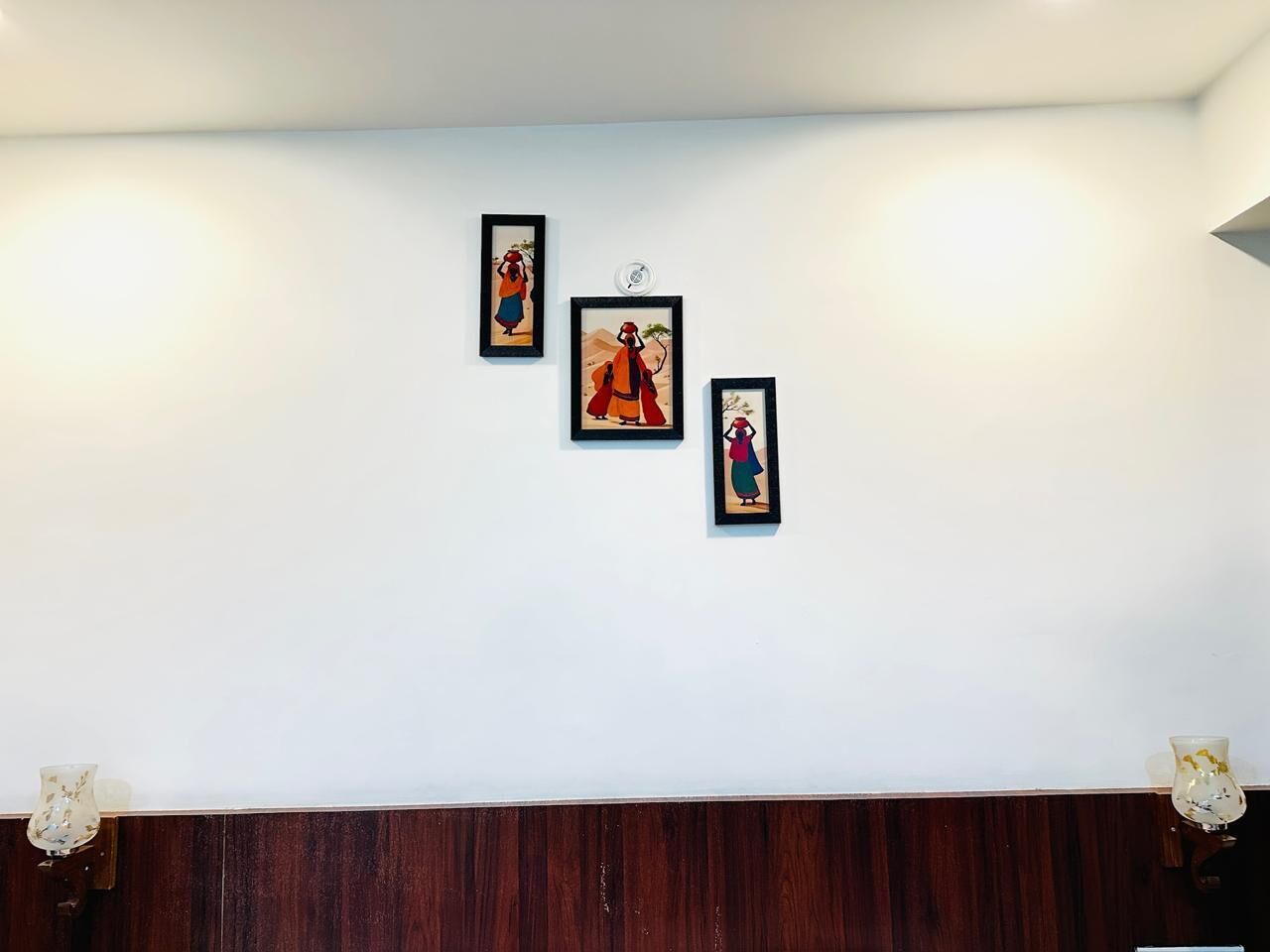 Habitación con pared blanca y panel de madera en la parte inferior. Tres cuadros enmarcados cuelgan de la pared.