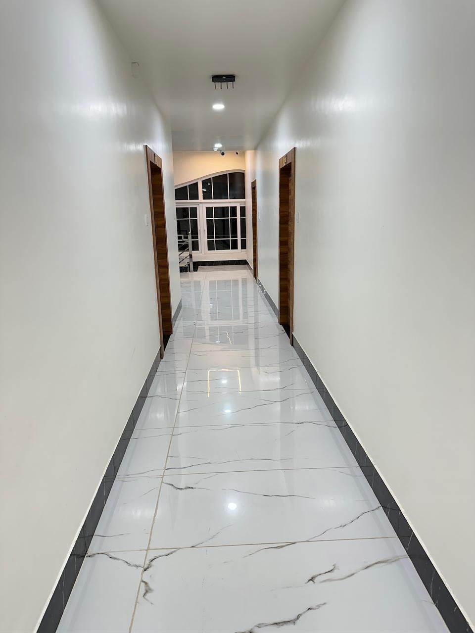 A hallway with white walls, a marble floor, and wooden doors.
